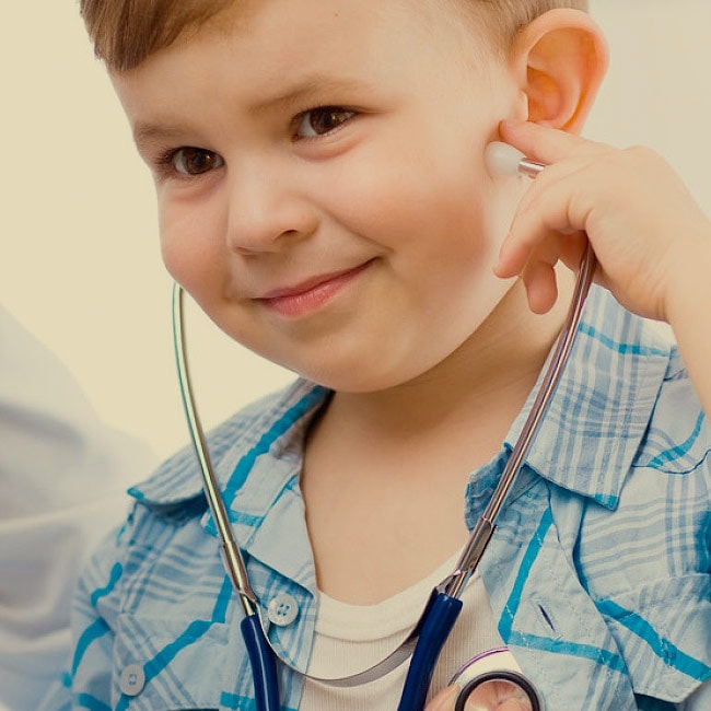 Ein lächelndes Kind hält sich spielerisch ein Stethoskop ans Ohr: ein freundlicher Hinweis auf medizinische Leitungen der Ostseeklinik Grömitz bei einer Mutter-Kind-Kur oder Vater-Kind Kur.