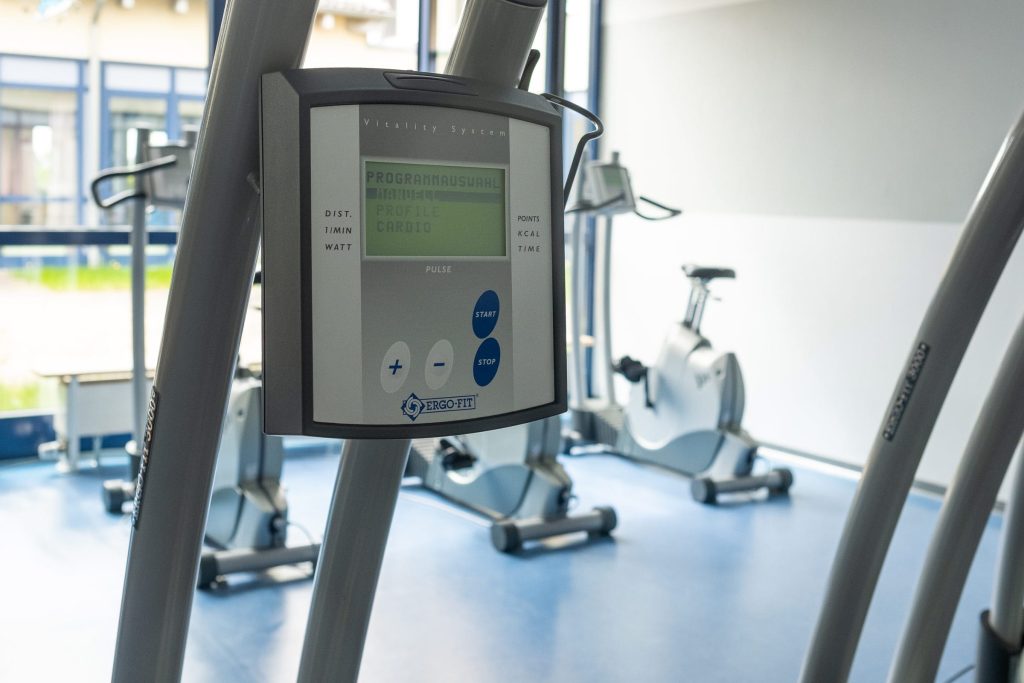Nahaufnahme des Bedienfelds eines Ergometers in einem hellen Trainingsraum der Ostseeklinik Grömitz. Im unscharfen Hintergrund sind weitere Fitnessgeräte vor einer Fensterfront zu sehen.