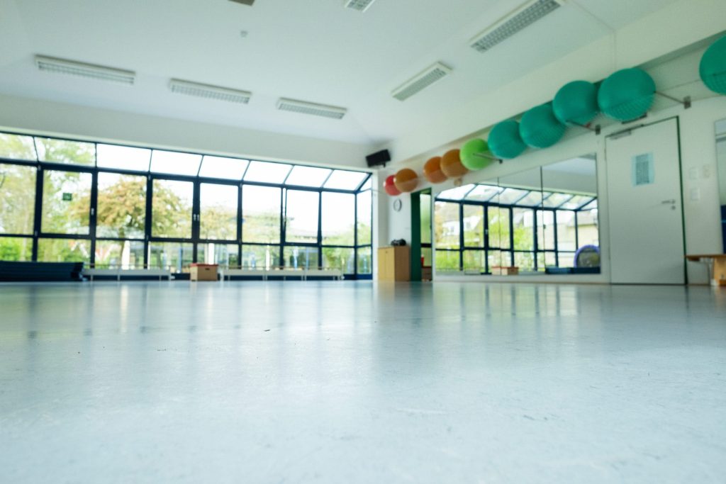 Ein heller, moderner Gymnastikraum in der Ostseeklinik Grömitz mit großer Fensterfront zum Grünen, hellem Sportboden und bunten Gymnastikbällen in einer Wandhalterung.