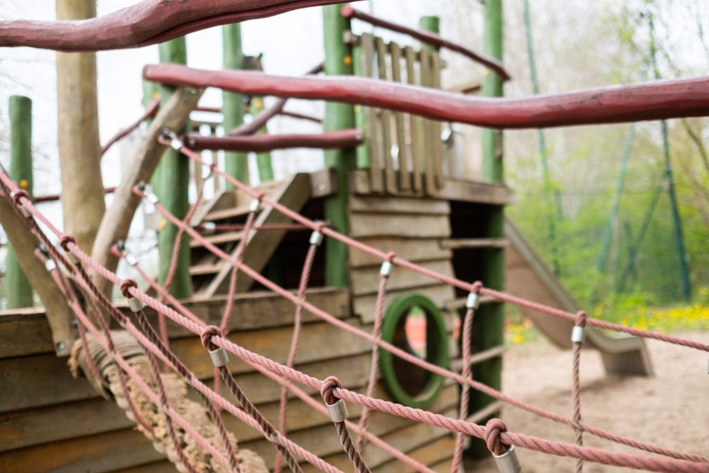 Hölzernes Kletterschiff mit Seilbrücke und Rutsche auf einem Kinderspielplatz im Außenbereich der Ostseeklinik Grömitz.