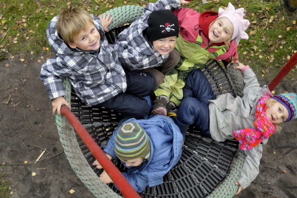 Fünf lachende Kinder spielen gemeinsam in einer großen Netzschaukel im Außenbereich der Ostseeklinik Grömitz.