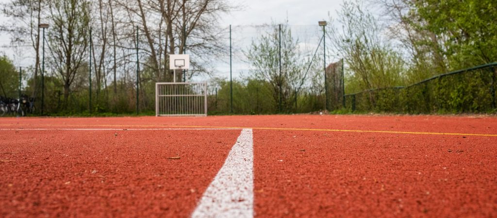 Nahaufnahme eines Sportplatzes mit rotem Belag, Fußballtor und Basketballkorb im Außenbereich der Ostseeklinik Grömitz.
