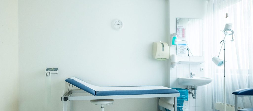 Hell eingerichtetes Behandlungszimmer in der Ostseeklinik Grömitz mit einer blauen Untersuchungsliege, Waschbecken und medizinischem Equipment.