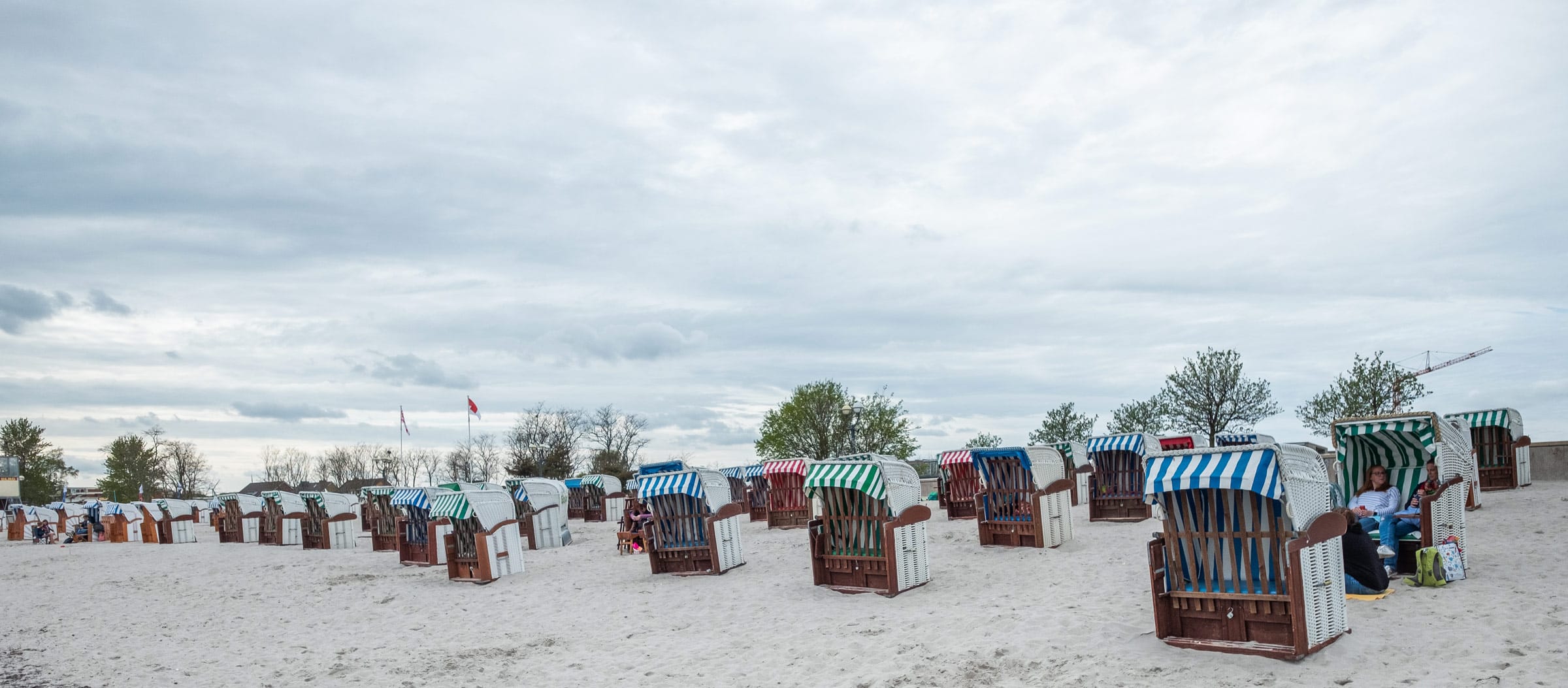 Zahlreiche blau, grün und rot gestreifte Strandkörbe stehen auf einem weitläufigen Sandstrand unter einem bewölkten Himmel an der Ostsee.