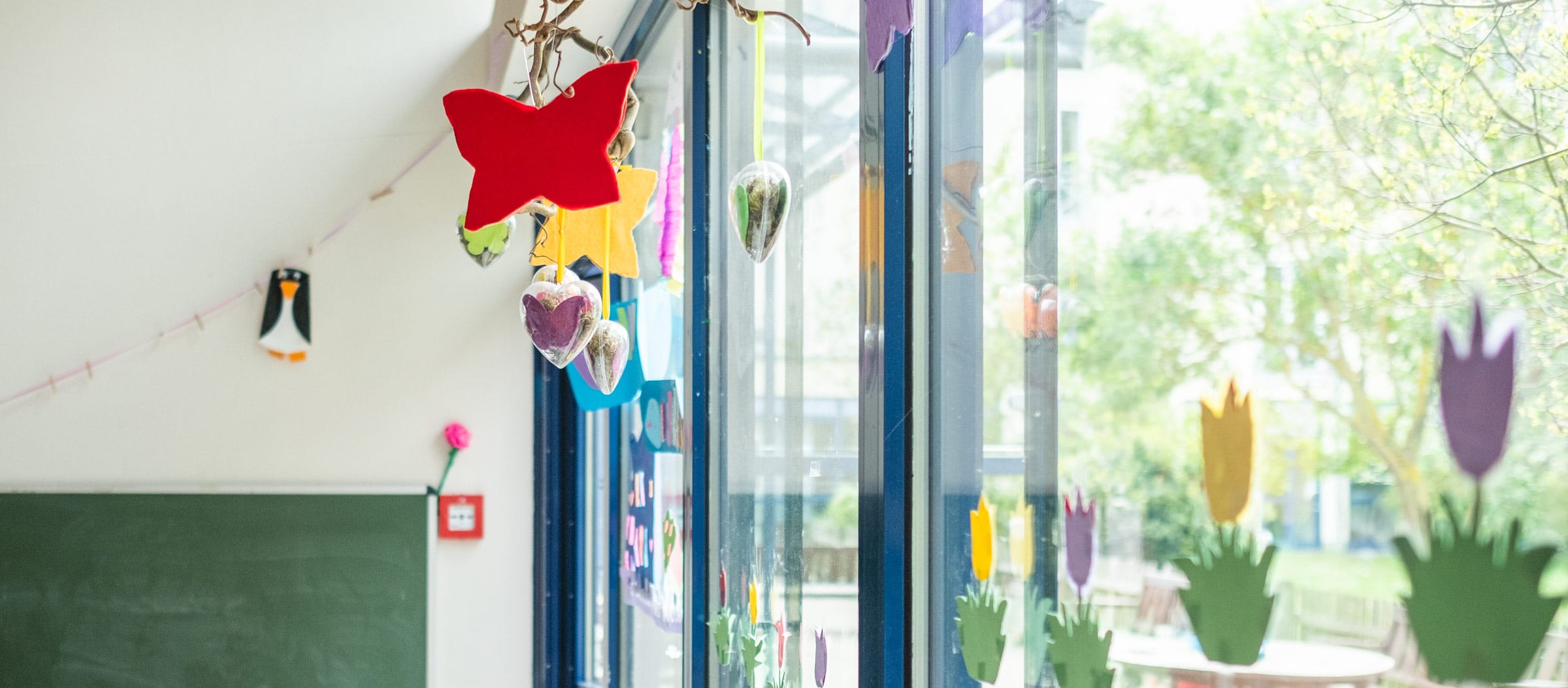 Heller, kindgerecht gestalteter Innenraum der Ostseeklinik Grömitz mit bunter Fensterdekoration aus Papierblumen und hängenden Bastelarbeiten, die eine freundliche Atmosphäre für Kinder schaffen.
