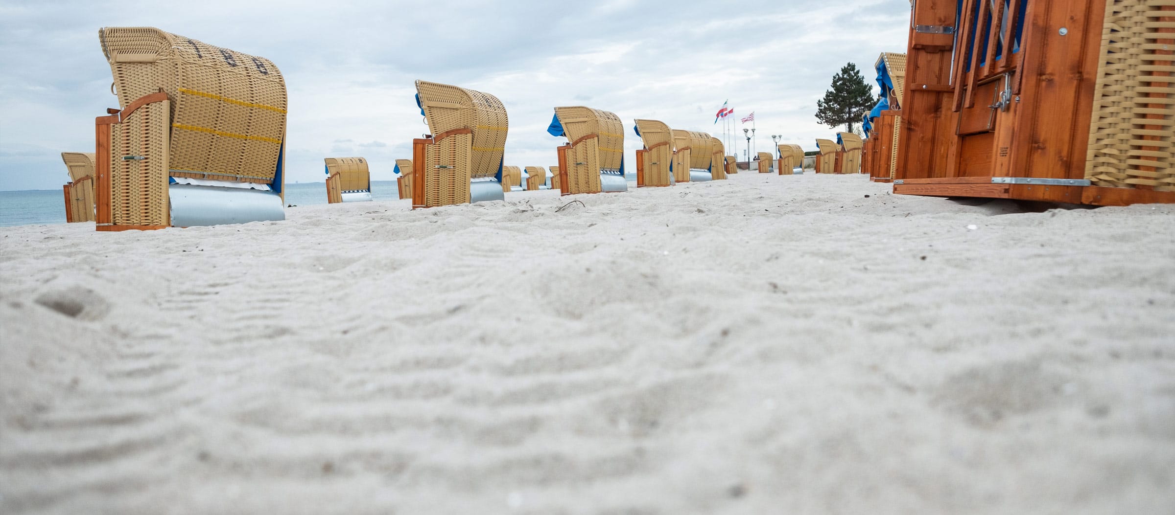 Eine Reihe von Strandkörben auf dem feinkörnigen, hellen Sandstrand von Grömitz unter einem bewölkten Himmel.