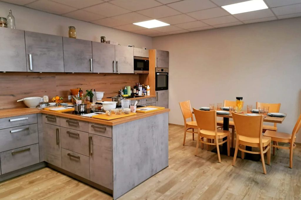Moderne Lehrküche in der Ostseeklinik Grömitz mit einer Kochinsel in Beton-Optik, Holz-Arbeitsplatten und einem angrenzenden Essbereich mit hellen Holzstühlen.