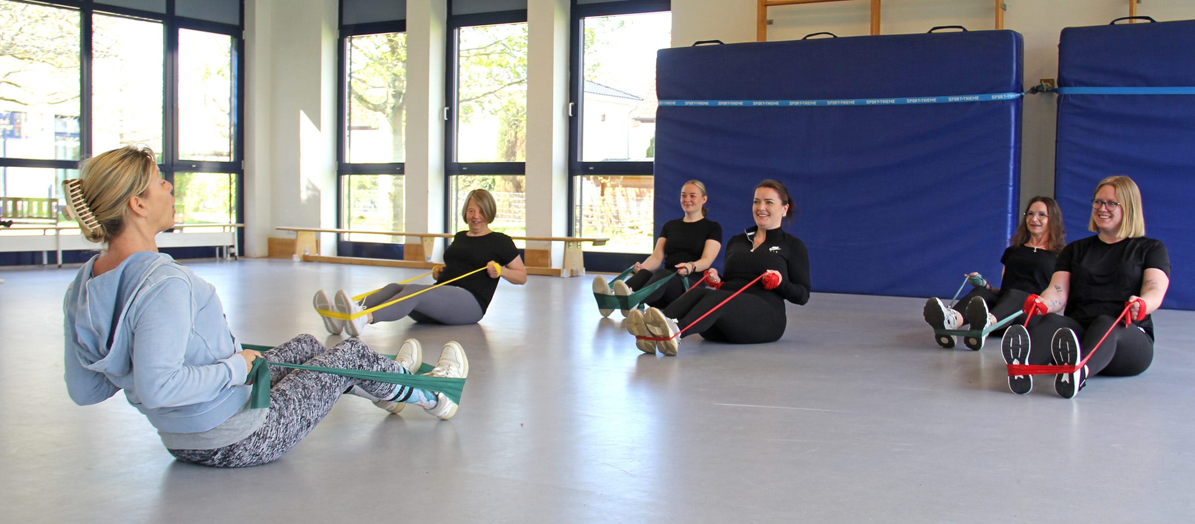 Eine Gruppe von Müttern nimmt an einem Sporttherapie-Kurs in der Gymnastikhalle der Ostseeklinik Grömitz teil. Unter Anleitung einer Trainerin führen die Teilnehmerinnen im Sitzen Kräftigungsübungen mit bunten Fitnessbändern durch
